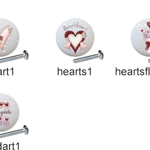 May include: Set of 7 ceramic drawer knobs with various designs, including a cat, hearts, flowers, a mouse, a ribbon, and a word art design. Each knob is white with pink and red accents. The knobs come with screws for installation.