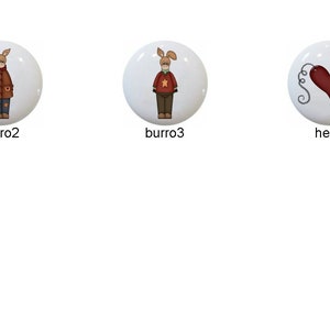 May include: Set of six ceramic knobs featuring various designs, including a donkey wearing a green coat, a donkey wearing a red coat, a donkey wearing a red sweater, a heart, a star, and a word art design that says "Boy Howdy It's Cold".