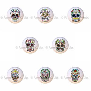 May include: Set of six colorful ceramic cabinet knobs featuring a sugar skull design. Each knob has a different floral pattern and is painted in bright colors.