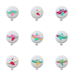May include: Fifteen ceramic knobs with airplane designs. Each knob features a different color scheme with green, pink, red, and yellow accents. The knobs are numbered 1 through 15.