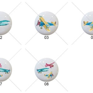 May include: Eight different ceramic knobs with airplane designs. The airplanes are painted in various colors, including blue, yellow, red, and pink. The knobs are round and white.