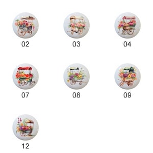 May include: Twelve ceramic knobs with floral cart designs. Each knob features a different arrangement of flowers and a cart with wheels. The knobs are white with a glossy finish.
