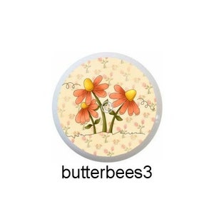 May include: Five round, colorful, ceramic buttons with a bee and butterfly design. The buttons feature a yellow bee with black stripes and a butterfly with different colored wings. The background of the buttons is a cream color with a floral pattern.