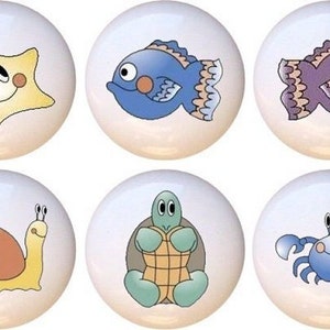 May include: Six ceramic knobs with different sea creature designs. The knobs feature a starfish, a blue fish, a purple fish, a snail, a turtle, and a crab.