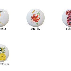 May include: Set of eight ceramic knobs featuring various floral and animal designs. The designs include a hibiscus flower, a kingfisher, a tiger lily, a paisley pattern, a crimson climbing rose, a trumpet flower, and two different paisley patterns.