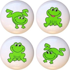 May include: Set of eight white ceramic cabinet knobs with green frog illustrations. The frogs are in different poses, including sitting, jumping, and upside down.