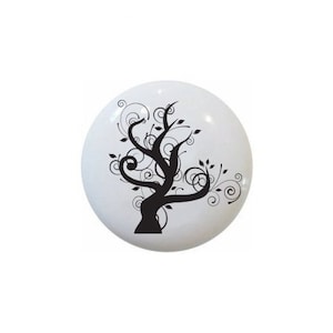 May include: A white ceramic knob with a black silhouette of a stylized tree with swirling branches and leaves.