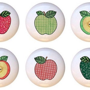 May include: Six ceramic knobs with different apple designs. The apples are red, green, and red and white plaid. One apple is cut in half and shows the inside of the apple. One apple has a green background with school supplies and the words "apple" and "school" written on it.