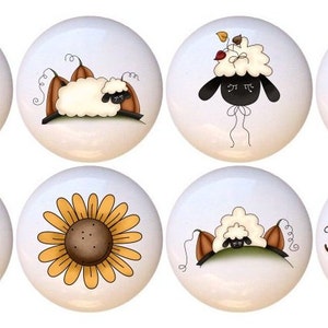 May include: Set of 6 ceramic knobs featuring a fall theme with sheep, pumpkins, sunflowers, and leaves. The knobs are white with colorful designs. One knob says "Fall is in the air".