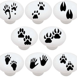 May include: Set of 10 white ceramic knobs with black paw prints, bear paw prints, and hand prints. The knobs are 1.5 inches in diameter.
