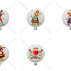 May include: Eight round ceramic knobs with colorful folk art designs. The designs include a man playing a horn, a woman in a red dress, a woman in a blue dress, a woman in a purple dress, a woman in a green dress, a woman with a basket of flowers, a woman with a basket of fruit, and a heart with flowers.