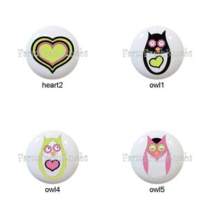 May include: A collection of eight white ceramic cabinet knobs. Designs include hearts and owls in various colors like black, pink, yellow, and green. Some knobs have text that reads "sweet hoots".