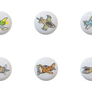 May include: Ten ceramic knobs with different cartoon airplane designs. The knobs are white with a glossy finish. The airplanes are in various colors, including green, yellow, blue, brown, and black.