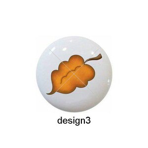 May include: Five different designs of ceramic knobs featuring autumn leaves in various colors and styles. The designs include a single red leaf, a single yellow leaf, a single orange leaf, a heart-shaped leaf, and a cluster of leaves on a vine.