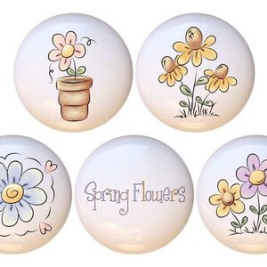 May include: Set of six ceramic knobs with spring flower designs. The knobs feature a variety of flowers in pink, yellow, purple, and blue. One knob has the text "Spring Flowers" in purple.