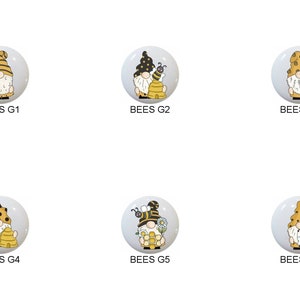 May include: Six round ceramic ornaments with a gnome design. Each gnome is wearing a yellow and black bee-themed hat and holding a bee or a honeycomb. The ornaments are labeled "BEES G1", "BEES G2", "BEES G3", "BEES G4", "BEES G5", and "BEES G6".