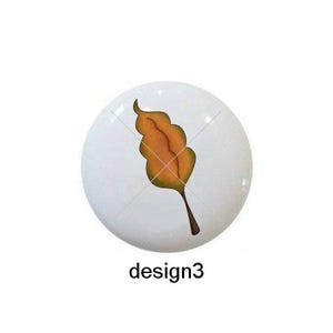 May include: Five different designs of round ceramic knobs with autumn leaf and branch designs. The designs include a black branch with white leaves, a single orange leaf, a single orange leaf with a pointed tip, two red leaves, and a branch with five yellow leaves.