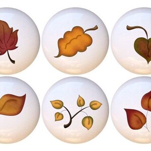 May include: Set of 10 ceramic knobs featuring autumn leaves in various shades of brown, orange, and yellow. The knobs are white with a glossy finish.