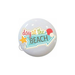 May include: A white round button with a blue arrow pointing to the right. The arrow has the text "day at the BEACH" in brown letters. The arrow is decorated with a yellow star and a red seashell.