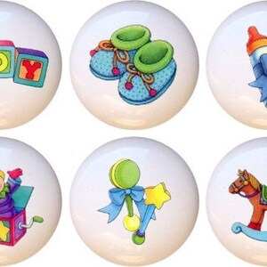 May include: Set of 10 ceramic knobs featuring colorful illustrations of baby toys, including a toy airplane, building blocks spelling "BOY", baby shoes, a baby bottle, a stroller, a jack-in-the-box, a rattle, a rocking horse, and a teddy bear with balloons.