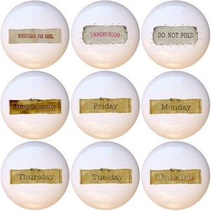 May include: Twelve white ceramic knobs with brown paper labels. The labels have various text, including "Laundry Room", "Do Not Fold", "Washable Casual", "Dirty Laundry", "Friday", "Monday", "Saturday", "Sunday", "Thursday", "Tuesday", "Wash Day", and "Wednesday".