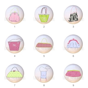 May include: Nine different ceramic knobs with various handbag designs. Each knob is white with a colorful handbag design. The designs include a pink and white plaid handbag, a green and white floral handbag, a black and white zebra print handbag, a pink and white polka dot handbag, a pink and white checkered handbag, a pink and white floral handbag, a pink and white striped handbag, a blue and white striped handbag, and a pink and white floral handbag.