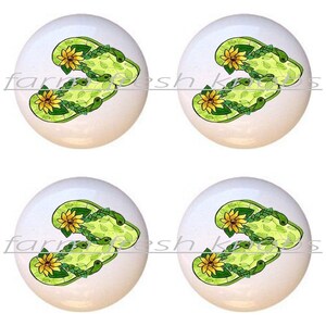 May include: Four white ceramic knobs with a green and yellow flip-flop design. Each knob features a pair of flip-flops with green leaves and yellow sunflowers.