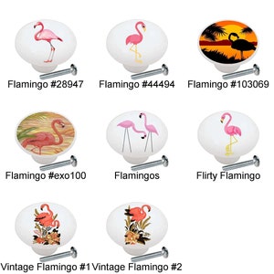May include: A collection of 12 ceramic cabinet knobs featuring pink flamingos in various poses and settings. The knobs are white with a glossy finish and have a silver screw for attachment.