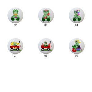 May include: Eleven round ceramic knobs with different green monster designs. The designs include a monster holding a flag, a monster holding a slice of watermelon, a monster holding a popsicle, a monster holding a stack of books, a monster holding a bunch of bananas, a monster holding a bunch of grapes, a monster holding a bunch of flowers, a monster holding a red apple, a monster holding a bunch of crayons, a monster holding a toy truck, and a monster holding a sun.