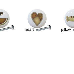May include: Five ceramic knobs with different designs: a cat, a watermelon with a bird, a heart, a pillow, and a sign. Each knob has a silver screw.