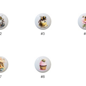 May include: A collection of eight white ceramic cabinet knobs, each featuring a unique bee-themed design. The designs include bumblebees, bees with teacups, and a cupcake with a bee. Each knob is numbered from #1 to #8.
