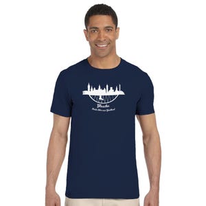 Op de afbeelding: Marineblauw t-shirt met een witte afbeelding van een skyline en de tekst "Glaschu" en "Baile Mòr nan Gàidheal". Het ontwerp is gecentreerd op de voorkant van het shirt.
