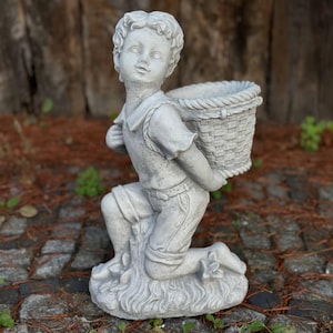 May include: A gray stone garden statue of a kneeling boy holding a woven basket. The boy is wearing a short-sleeved shirt and shorts. The statue is on a stone surface with a wooden background.