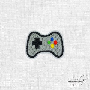 Könnte beinhalten: Gestickter Aufnäher mit einem grauen Videospiel-Controller mit schwarzer Umrandung. Der Controller hat ein schwarzes kreuzförmiges Steuerkreuz und farbige Knöpfe in Blau, Grün, Rot und Gelb. Der Aufnäher befindet sich auf einem weißen Stoffhintergrund.