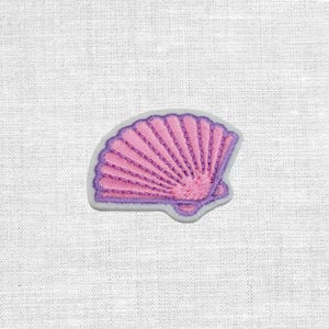 Könnte beinhalten: Ein pinkfarbener, gestickter Muschelaufnäher mit lila Umrandung. Das Muscheldesign weist detaillierte Nähte und eine hellrosa Farbe auf, vor einem weißen Hintergrund.
