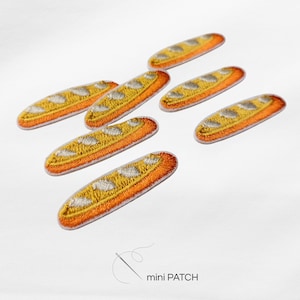 Könnte beinhalten: Sechs gestickte Aufnäher in Form von Baguettes, jeder mit einer goldgelben Kruste, weißen diagonalen Einschnitten und orangefarbenen Schattierungen. Die Aufnäher sind verstreut angeordnet, und der Text mini PATCH ist darunter zu sehen.