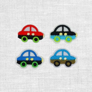 Könnte beinhalten: Vier gestickte Autoaufnäher in Rot, Schwarz, Blau und Braun. Jedes Auto hat ein weißes Fenster und grüne oder blaue Räder. Die Aufnäher befinden sich auf einem weißen Stoffhintergrund.