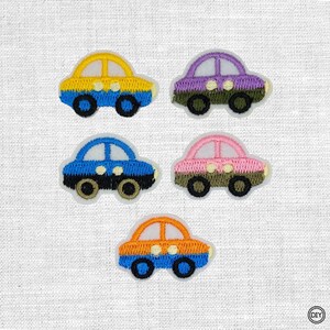 Könnte beinhalten: Fünf gestickte Auto-Aufnäher in einer Anordnung. Das Auto oben links ist gelb und blau, oben rechts lila und grün, in der Mitte links blau und schwarz, in der Mitte rechts rosa und grün und das untere Auto ist orange und blau.