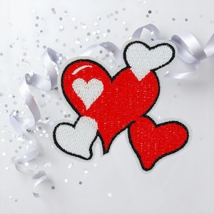 Könnte beinhalten: Gestickte Herz-Patches in Rot und Weiß mit schwarzen Umrissen, angeordnet auf einer weißen Oberfläche. Silbernes Konfetti und weiße Bänder ergänzen die Dekoration. Ideal für Valentinstag oder andere romantische Anlässe. Geeignet zum Aufnähen.