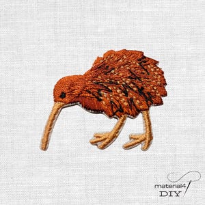 Könnte beinhalten: Ein gestickter Aufbügler in Form eines Kiwis im Profil. Der Vogel hat einen runden Körper mit strukturierten orangefarbenen und braunen Federn, einen langen, dünnen, hellen Schnabel und zwei helle Beine. Das Design ist mit schwarzen Stichen detailliert.