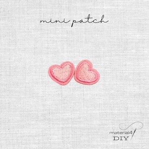 Könnte beinhalten: Zwei rosa herzförmige, gestickte Aufnäher mit hellrosa Umrandung. Der Text "mini patch" befindet sich über den Herzen. In der unteren rechten Ecke steht der Text "material4 DIY". Die Aufnäher befinden sich auf einem weißen, strukturierten Stoff.