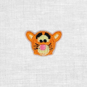 Könnte beinhalten: Gestickter Aufnäher mit dem Gesicht von Tigger aus Winnie the Pooh. Der Aufnäher hat orangefarbenes Fell mit schwarzen Streifen, schwarze Augenbrauen und eine rosa Nase. Der Aufnäher befindet sich auf weißem Hintergrund.