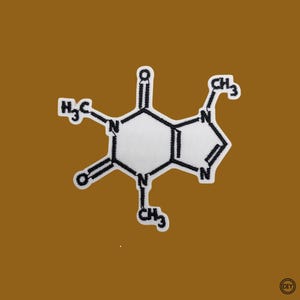 Könnte beinhalten: Weiß-schwarzer, gestickter Aufnäher mit der Molekülstruktur von Koffein. Der Aufnäher hat die Form des Koffeinmoleküls, wobei die chemische Formel sichtbar ist. Auf braunem Hintergrund.