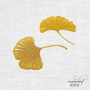 Könnte beinhalten: Zwei goldene Ginkgo-Blatt-Stickaufnäher mit detaillierten Fadenstichen und markanten fächerförmigen Silhouetten. Die Stickerei zeigt eine leuchtend goldgelbe Farbe mit sichtbaren Adernmustern, die vom Stiel bis zu den Rändern verlaufen.