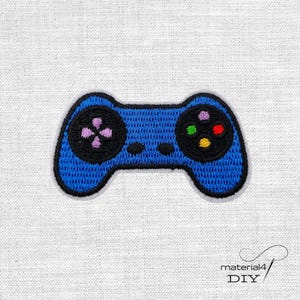 Könnte beinhalten: Gestickter blauer Videospiel-Controller-Patch mit schwarzem Rand. Der Controller hat ein Richtungspad mit lila Knöpfen und farbigen Aktionstasten. Der Patch befindet sich auf einem weißen Stoffhintergrund. Der Text "material4 DIY" befindet sich unten rechts.