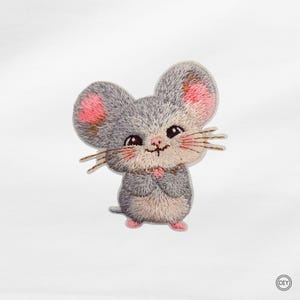 Könnte beinhalten: Ein gestickter Aufnäher in Form einer grauen Maus mit großen Ohren, rosa Innenohren und einem hellbeigen Bauch. Die Maus hat dunkle Augen, eine kleine rosa Nase und braune Schnurrhaare. Ein kleines kreisförmiges Logo mit dem Text DIY ist zu sehen.