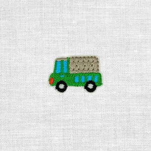Könnte beinhalten: Gestickter Aufnäher eines grünen Lastwagens mit einem beigefarbenen Laderaum, blauen Fenstern und schwarzen Rädern. Der LKW hat eine rote Frontstoßstange und ist weiß umrandet. Der Aufnäher befindet sich auf einem weißen Stoffhintergrund.