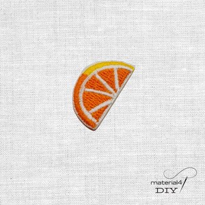Könnte beinhalten: Ein gestickter Aufnäher in Form einer Orangenscheibe. Das Design zeigt ein leuchtend orangefarbenes Fruchtsegment mit gelber Schale und weißen Stickereien, die die inneren Abschnitte der Frucht detailliert darstellen. Der Aufnäher hat einen sauberen Rand.