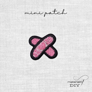 Könnte beinhalten: Ein gestickter Mini-Aufnäher mit zwei gekreuzten, rosafarbenen Heftpflastern mit schwarzem Rand. In der Mitte der Pflaster befindet sich ein kleines rosa Herz. Der Text mini patch steht darüber und material4 DIY steht darunter.