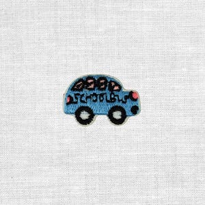 Könnte beinhalten: Ein blaues, gesticktes Abzeichen in Form eines Schulbusses. Der Aufnäher hat schwarze Räder, eine weiße Kontur und die Worte "SCHOOL BUS" in handschriftlicher Form. Der Bus hat rosa Akzente und ein paar Figuren im Inneren.